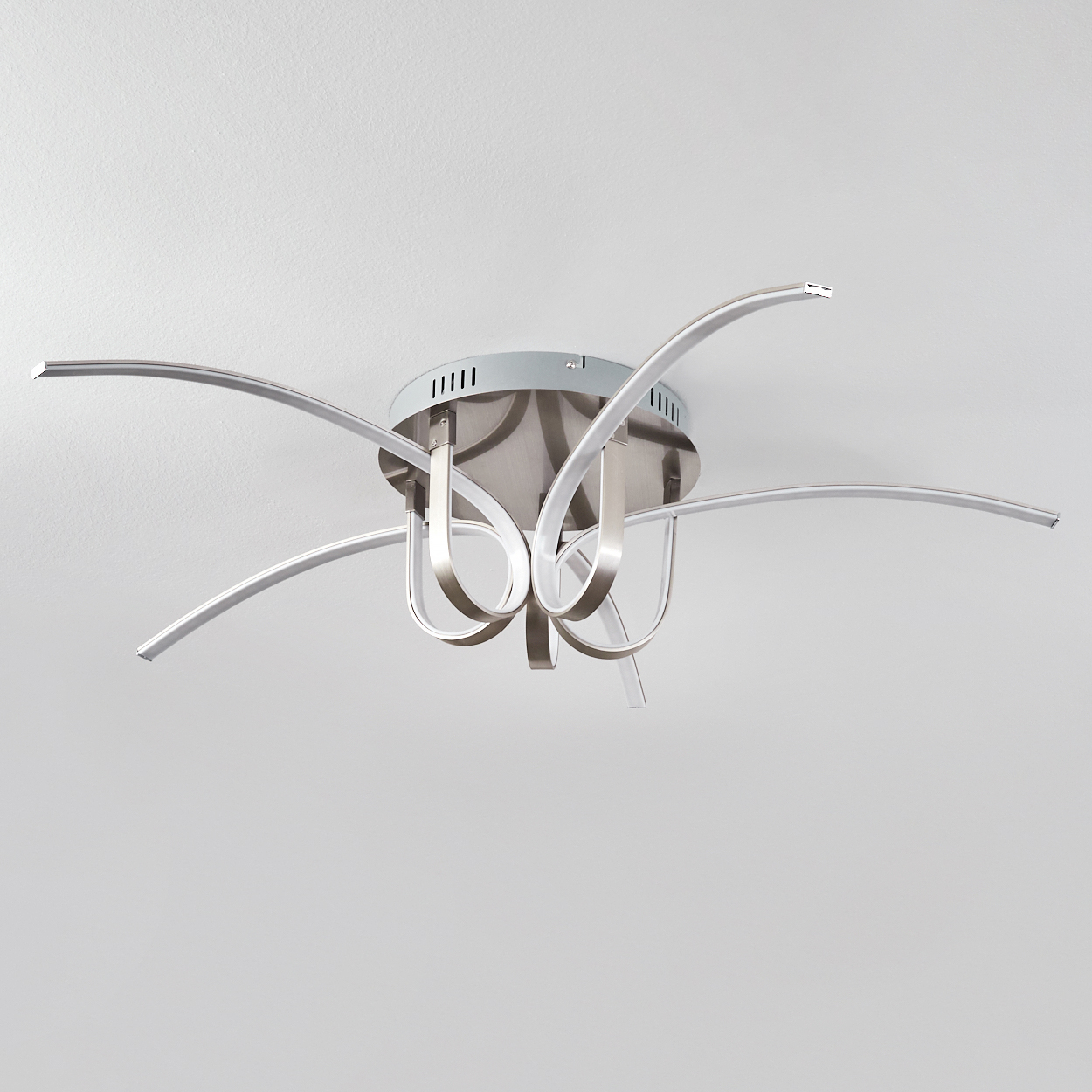 Deckenlampe mit silbernem Rahmen und geschwungenen Armen. Der Hintergrund ist eine schlichte weiße Decke.