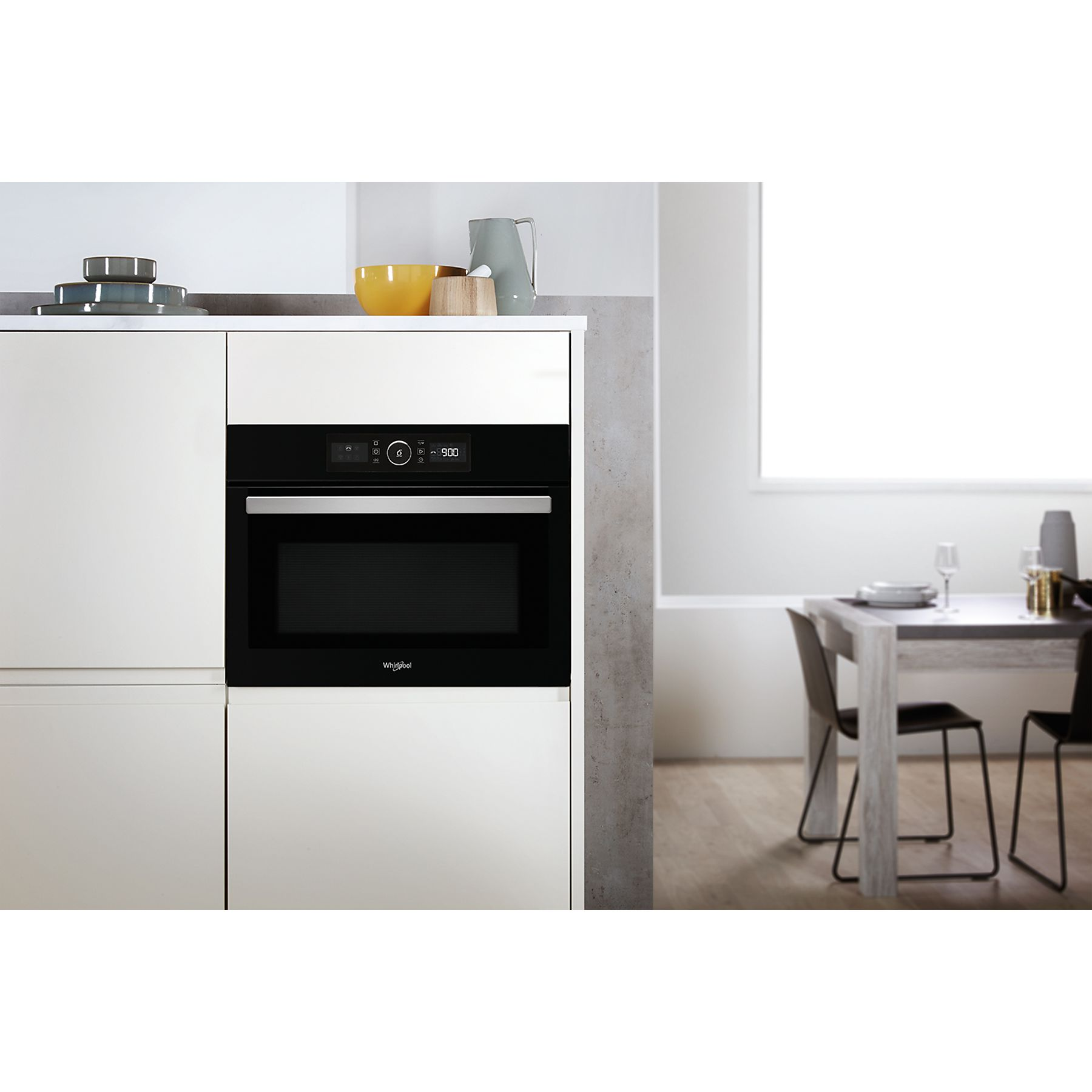 Un forno a microonde Whirlpool è installato in un mobile da cucina bianco, vicino a un tavolo da pranzo e sedie.