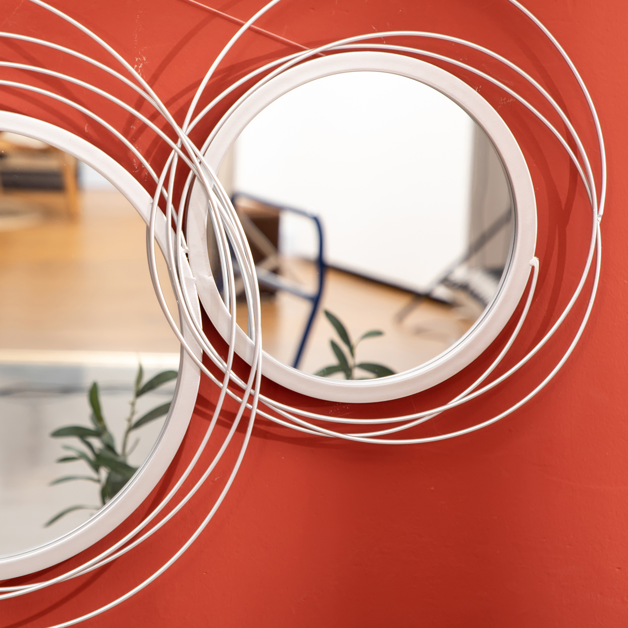 Nahaufnahme von zwei runden Spiegeln mit weißen Rahmen und roter Wand im Hintergrund. Pflanzen sind sichtbar.