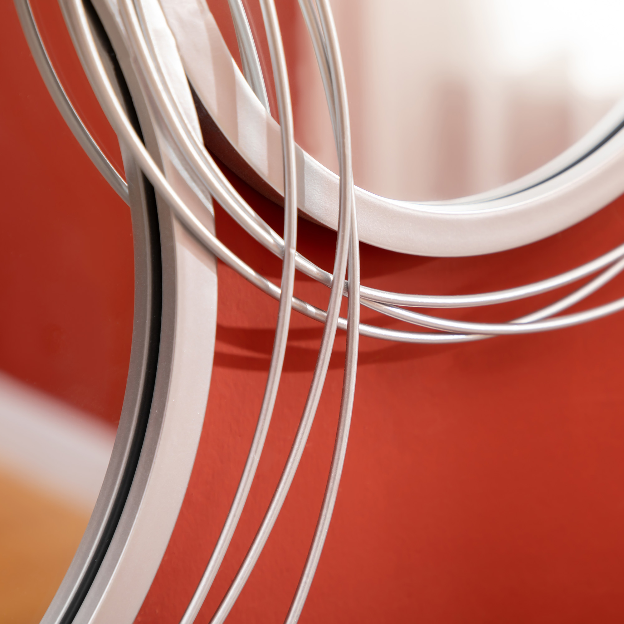 Nahaufnahme des silbernen Spiegels auf roter Wand. Der Rahmen hat ein einzigartiges, wellenförmiges Design.