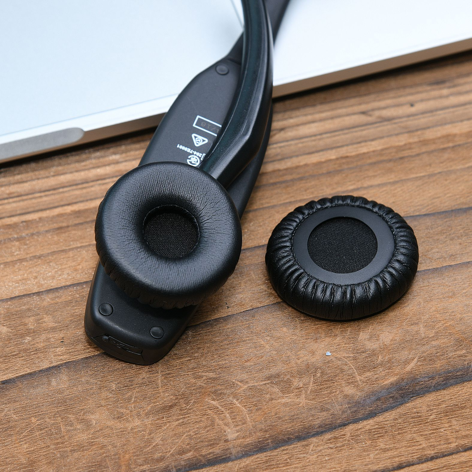 Ein Headset mit einem schwarzen Ohrpolster und einem zweiten daneben. Holzoberfläche im Hintergrund.