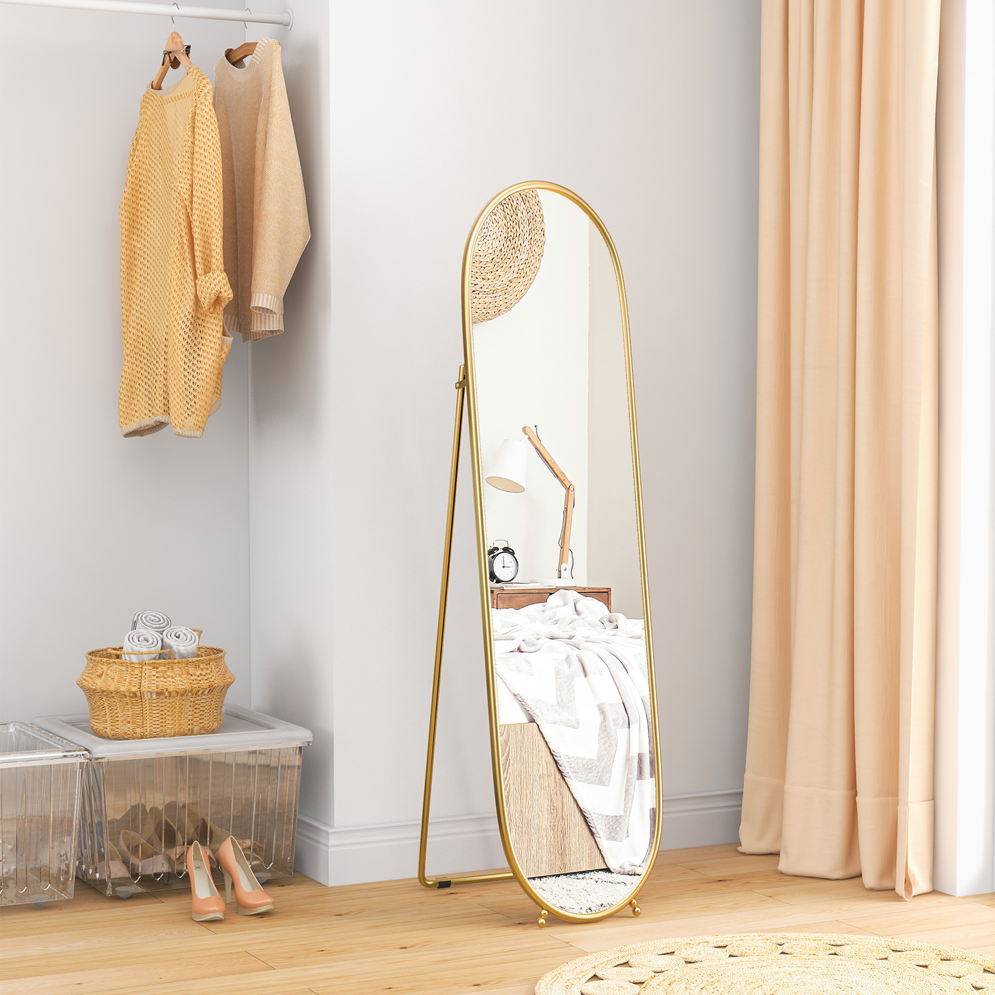 Ein Ganzkörperspiegel mit goldenem Rahmen. Er reflektiert ein Schlafzimmer mit Kleidung und Möbeln.