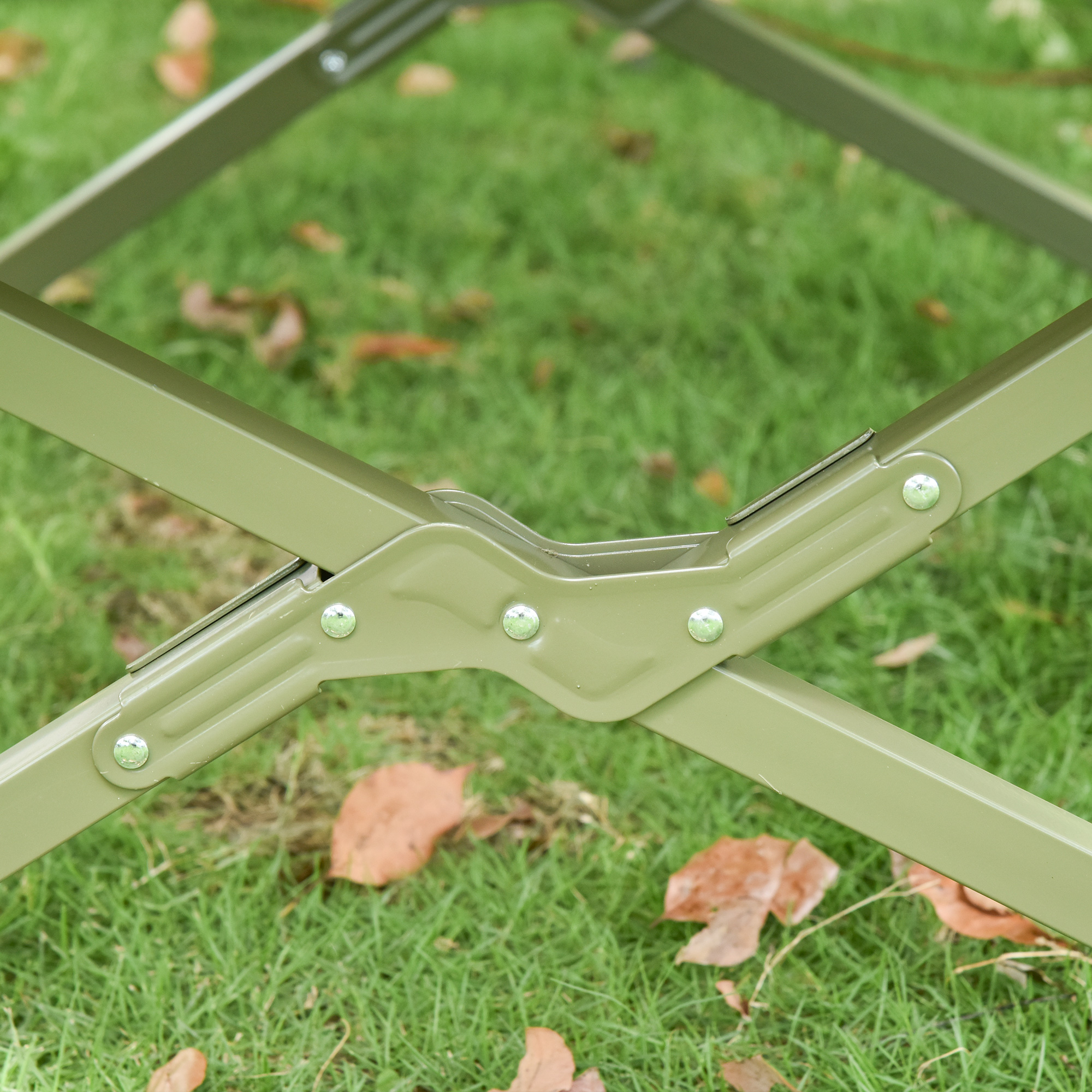 Nahaufnahme eines Metallgelenks eines Klappbetts. Die Farbe ist olivgrün, auf grünem Gras.