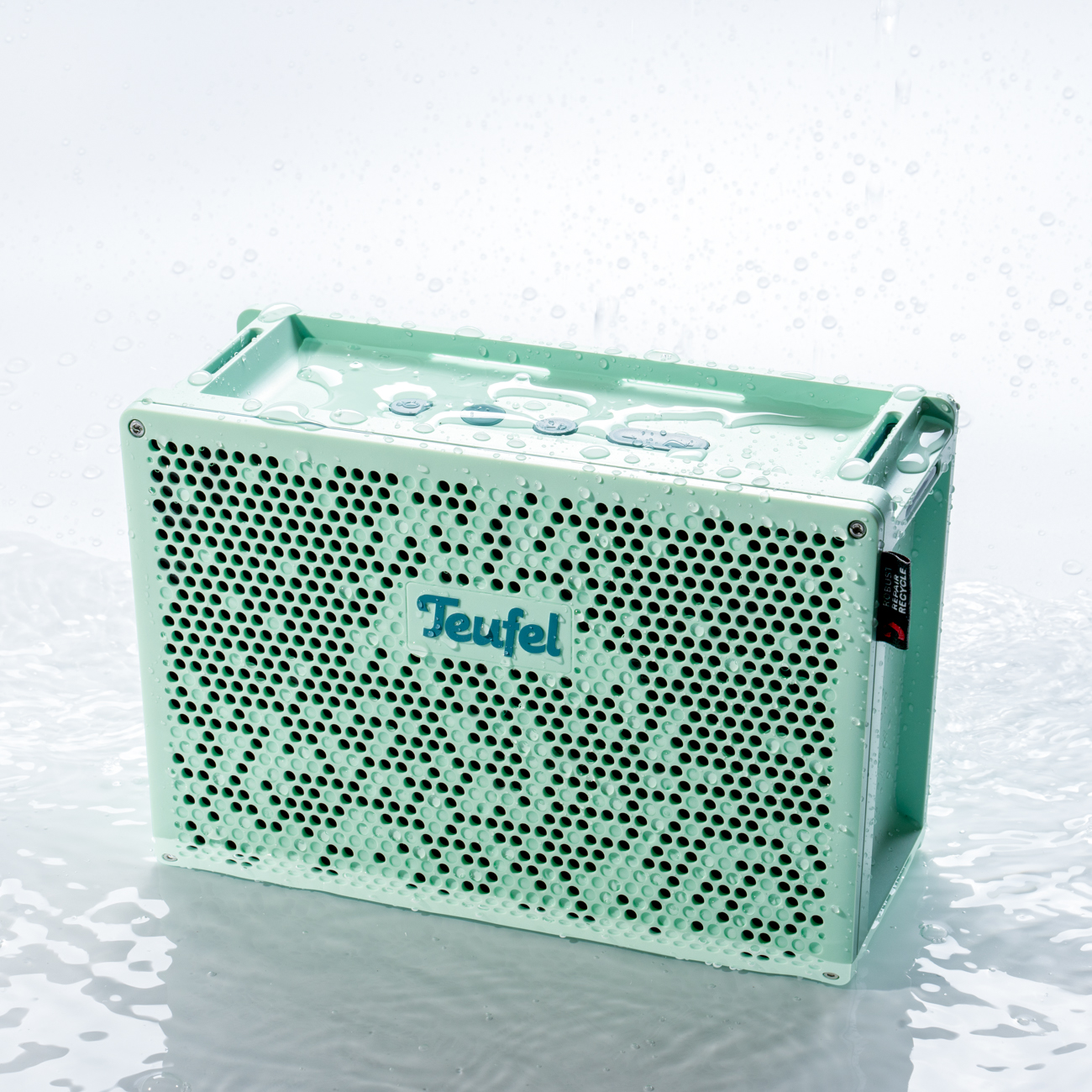 Un haut-parleur Teufel vert menthe avec des gouttelettes d'eau. Il a une face perforée et une poignée.