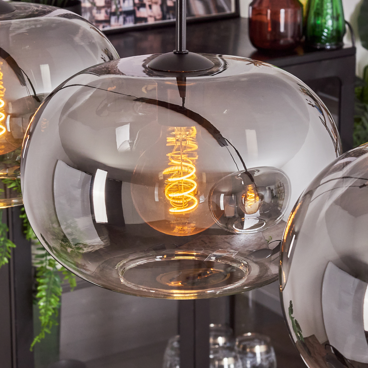 Nahaufnahme einer silbernen Kugelleuchte mit eingeschalteter Glühbirne. Der Hintergrund ist verschwommen und zeigt weitere Lichter.