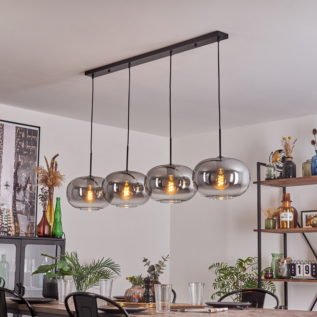 Ein Esszimmer mit Holztisch, Pendelleuchten und einem schwarzen Regal mit Dekorationsartikeln.