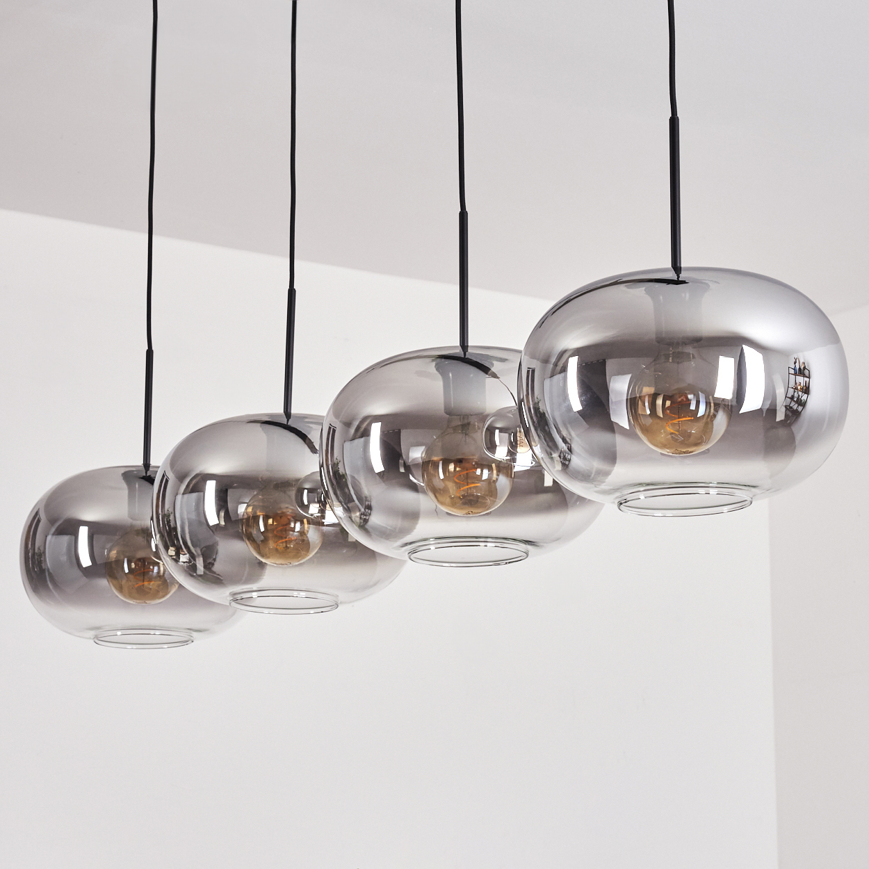 Vier Pendelleuchten mit kugelförmigen Glasschirmen hängen von einer weißen Decke.