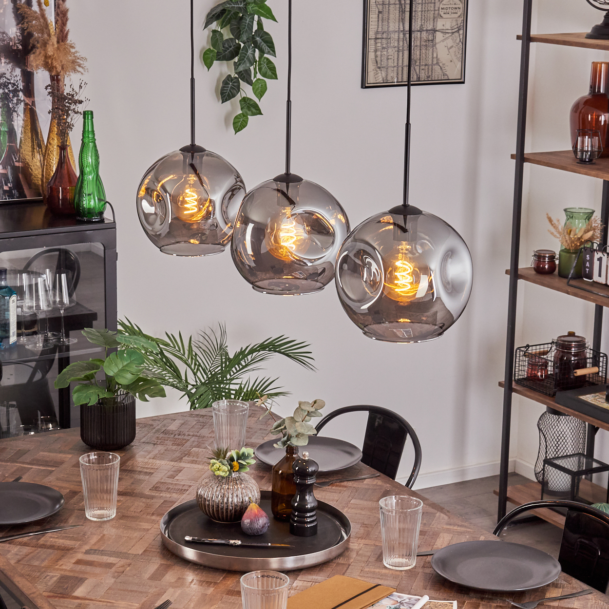 Ein Esszimmer mit Holztisch, drei Pendelleuchten und Dekorationsartikeln auf einem Regal.