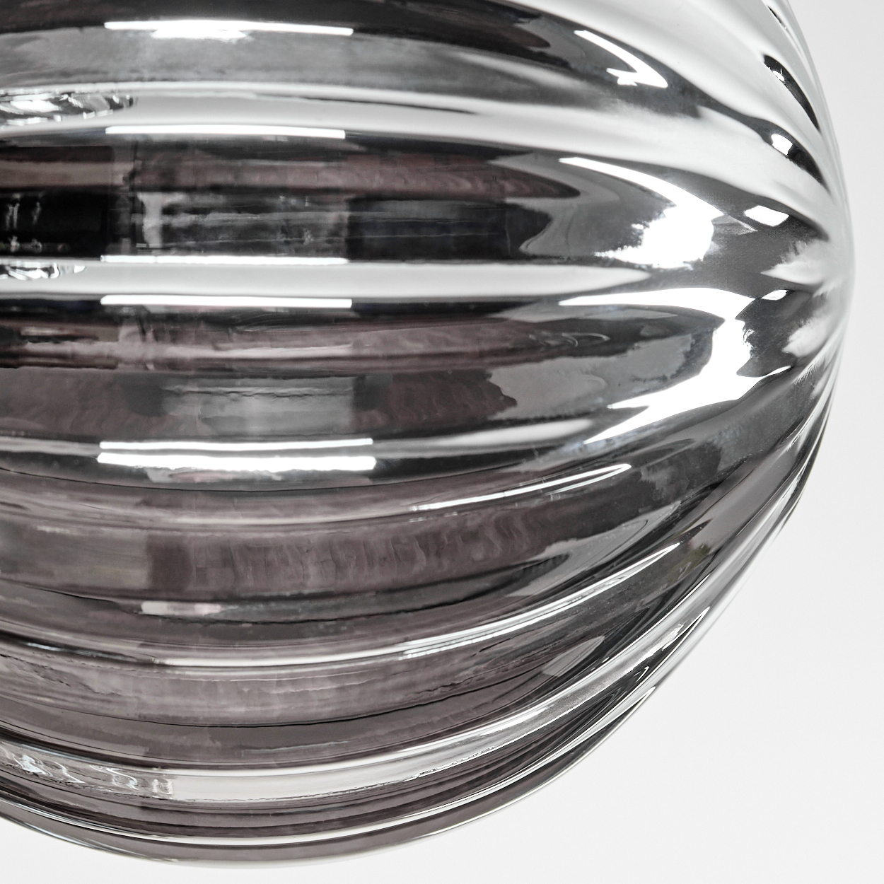 Nahaufnahme eines klaren, gerippten Glaslampenschirms. Das Glas reflektiert Licht und umgebende Objekte, was eine glänzende Oberfläche erzeugt.