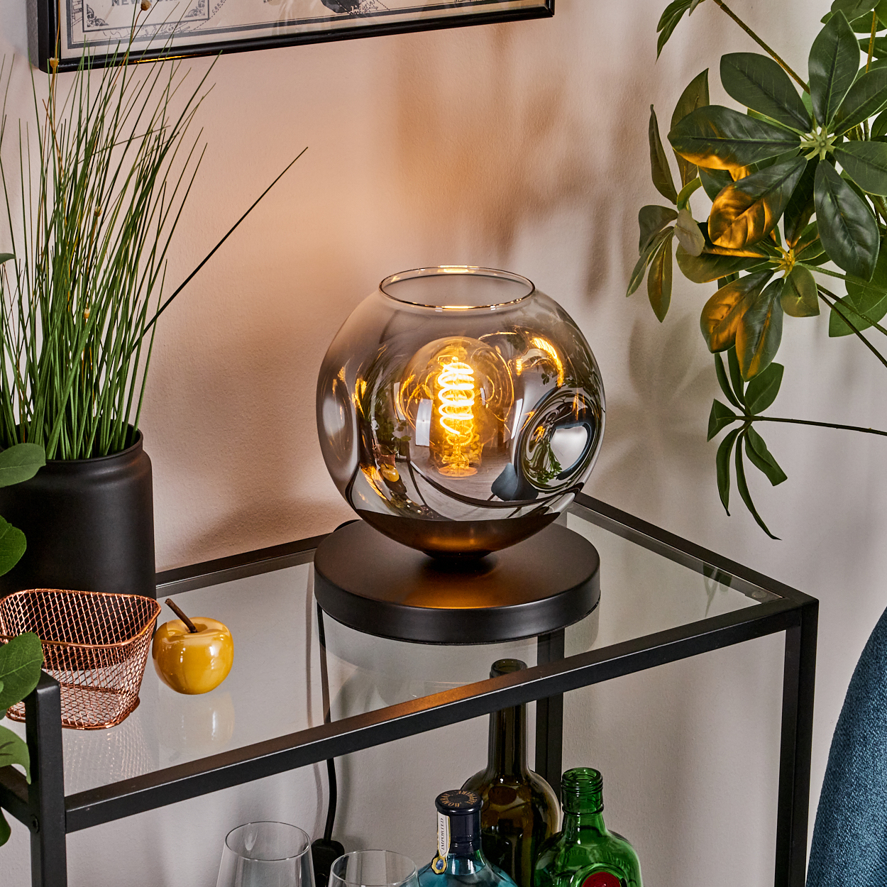 Eine Lampe mit reflektierendem, kugelförmigem Schirm, platziert auf einem Tisch mit Dekoration, zeigt eine Glühbirne.