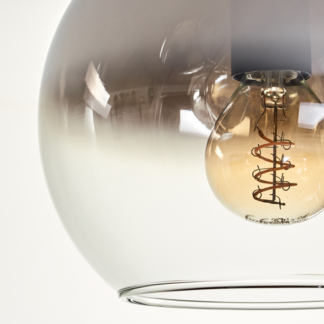 Nahaufnahme einer Pendelleuchte. Eine Glühbirne befindet sich in einer Glaskugel mit Metallic-Finish.