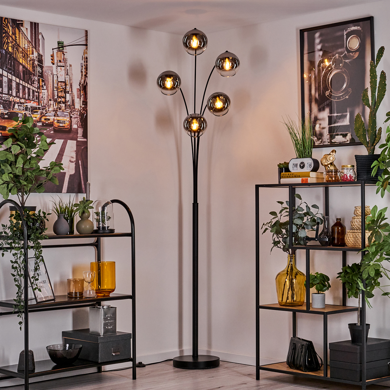 Eine Stehlampe mit fünf kugelförmigen Schirmen, umgeben von Regalen, Pflanzen und Stadtkunst.