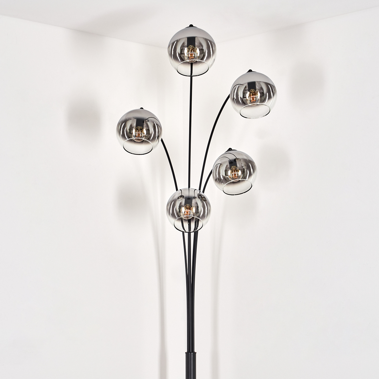 Eine Stehlampe mit fünf verchromten, kugelförmigen Schirmen, in einer Ecke platziert, weißer Wandhintergrund.