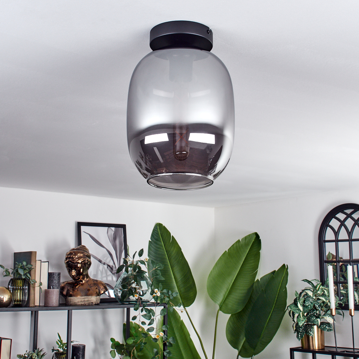 Deckenleuchte mit Glasschirm und sichtbarer Glühbirne. Das Licht ist in einem Raum mit Regalen und Dekoration.