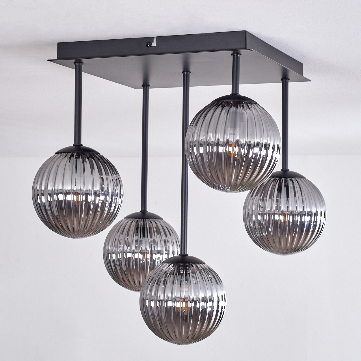 Eine Deckenlampe mit 5 silbernen Kugelschirmen, beleuchtet mit schwarzem Rahmen. Der Hintergrund ist weiß.