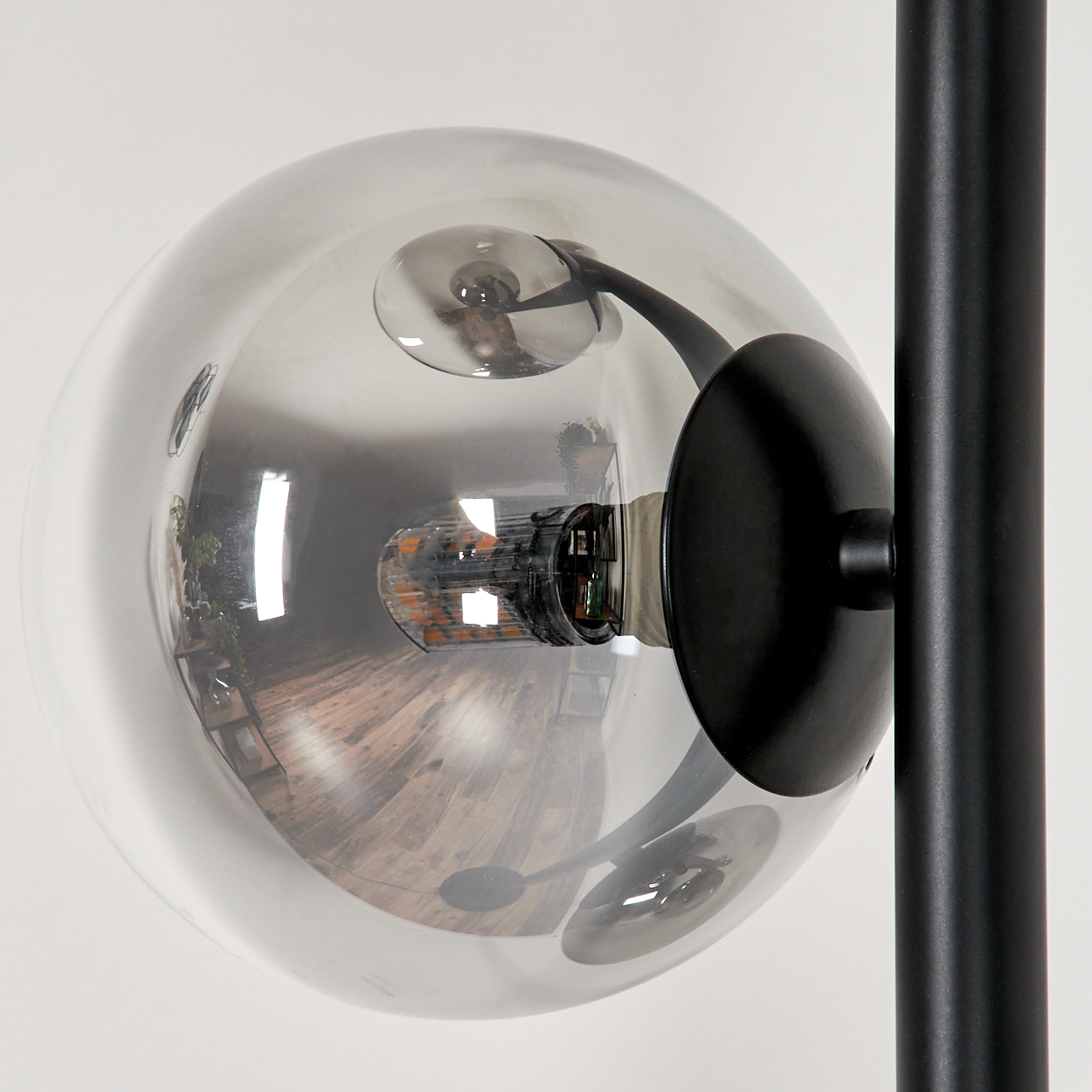 Nahaufnahme einer Glaskugelleuchte. Das Licht reflektiert ein Interieur und einen Holzboden.