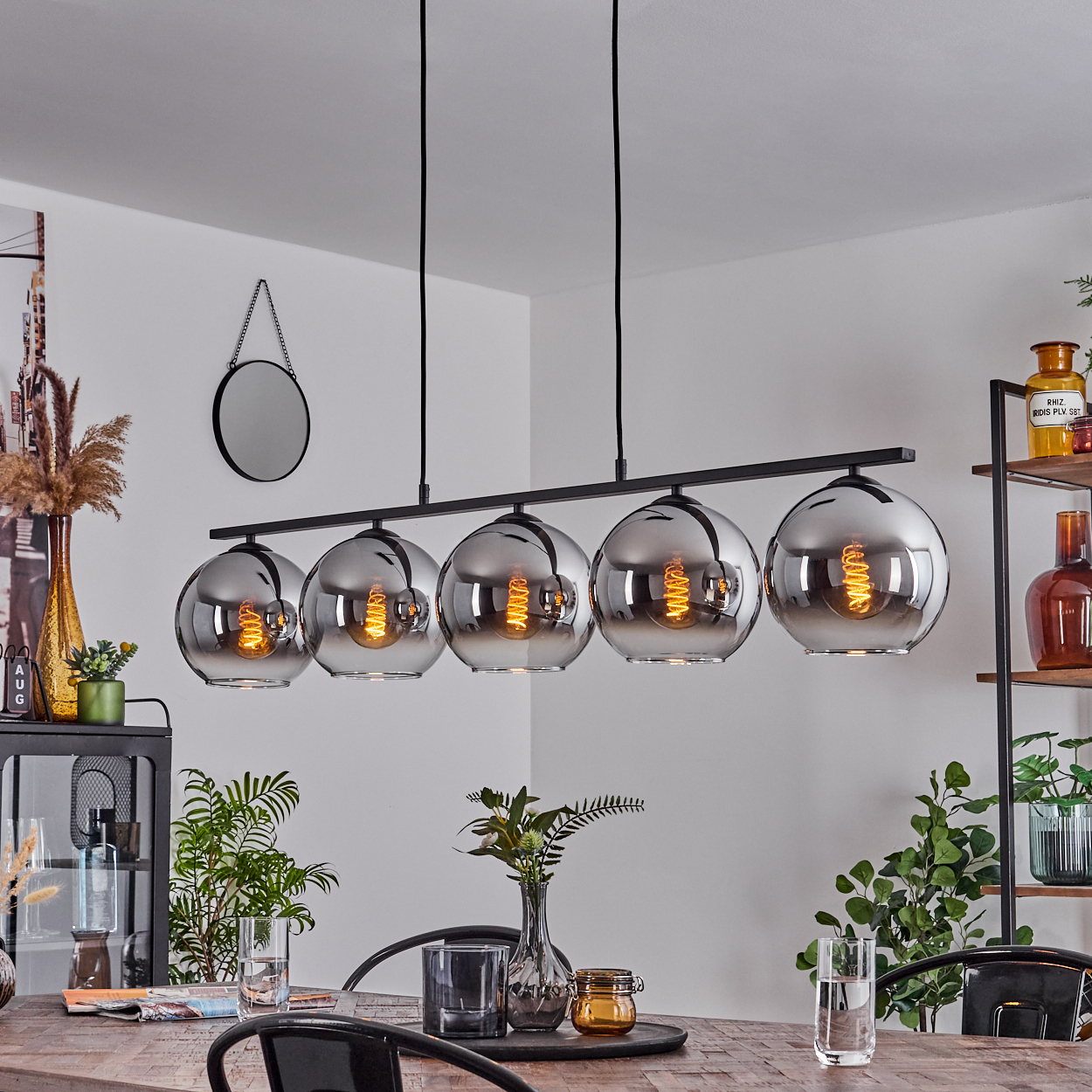 Ein schwarzer Kronleuchter mit fünf Glaskugeln mit sichtbaren Glühbirnen. Esszimmer mit Pflanzen und Dekorationen.