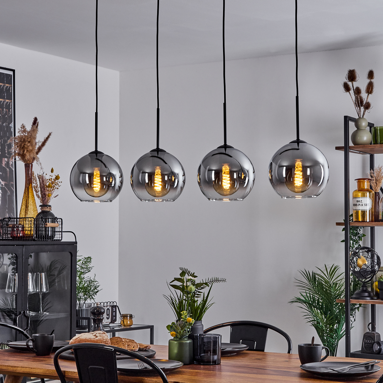Ein Esszimmer mit einem Holztisch und vier Hängelampen mit silbernen Schirmen. Schwarze Teller und Dekoration.