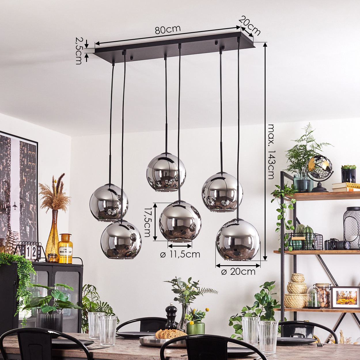Esszimmer mit Holztisch, Hängeleuchten und Maßen. Die Leuchten haben silberne Kugeln. Pflanzen sind im Bild.