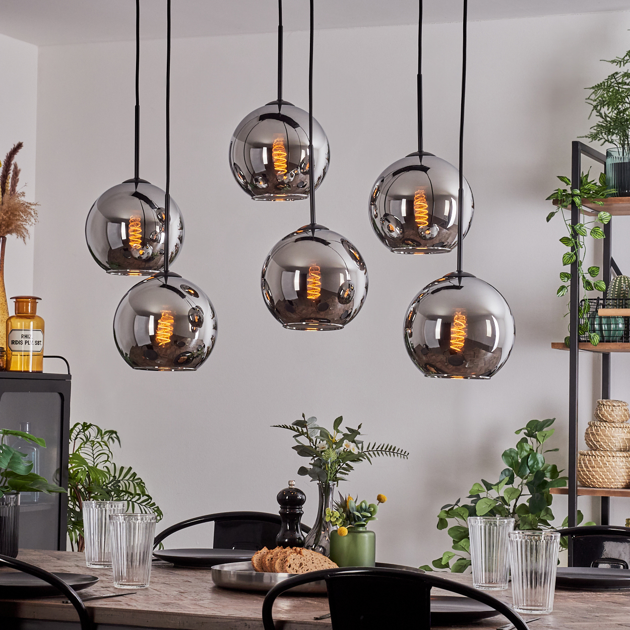 Esszimmer mit sechs Kugelleuchten über einem Holztisch. Pflanzen und Glaswaren sind ebenfalls sichtbar.
