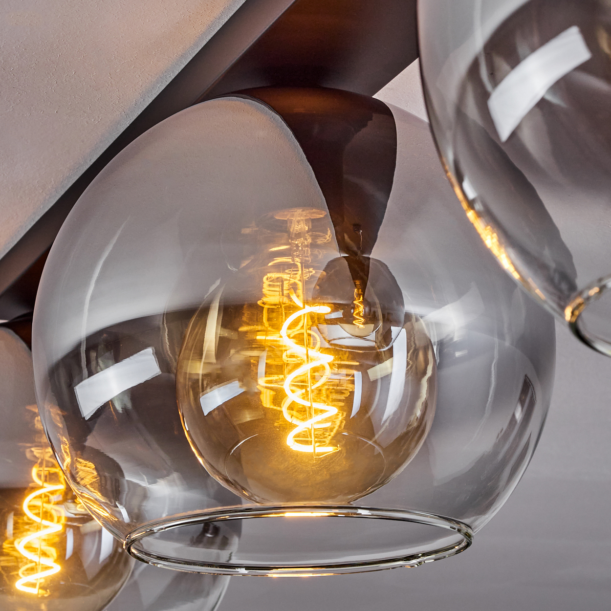 Nahaufnahme einer Glühbirne in einer transparenten, silberfarbenen Pendelleuchte. Die Glühbirne leuchtet mit warmem Licht.