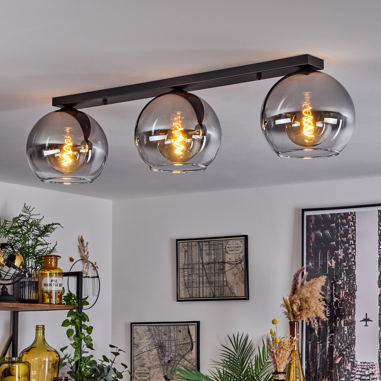 Drei silberne Pendelleuchten hängen von der Decke. Die Lichter sind an und beleuchten den Raum. Der Hintergrund zeigt Kunstwerke.