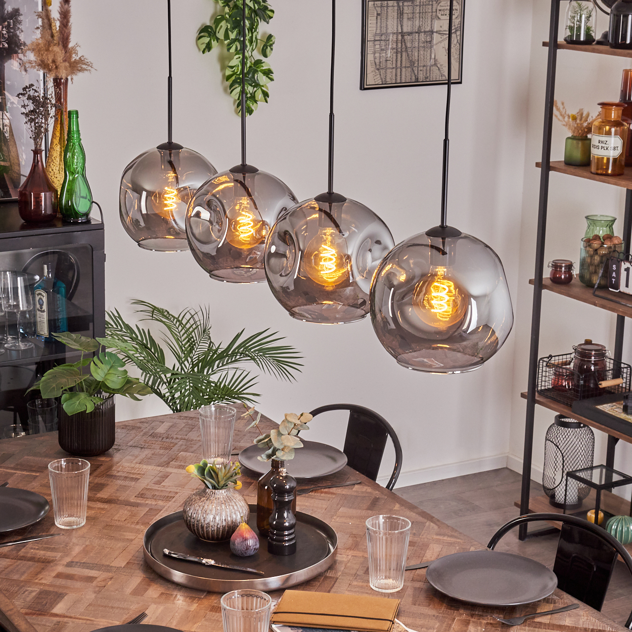 Vier Pendelleuchten mit grauen Glasschirmen hängen über einem Holztisch. Der Raum hat ein modernes Esszimmer-Setup.