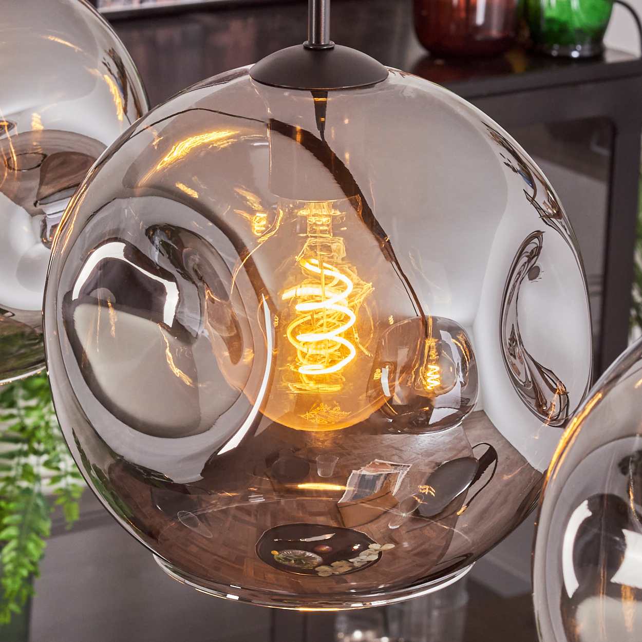 Nahaufnahme einer Pendelleuchte mit grauem Glasschirm. Eine spiralförmige Glühbirne leuchtet gelb im Inneren.
