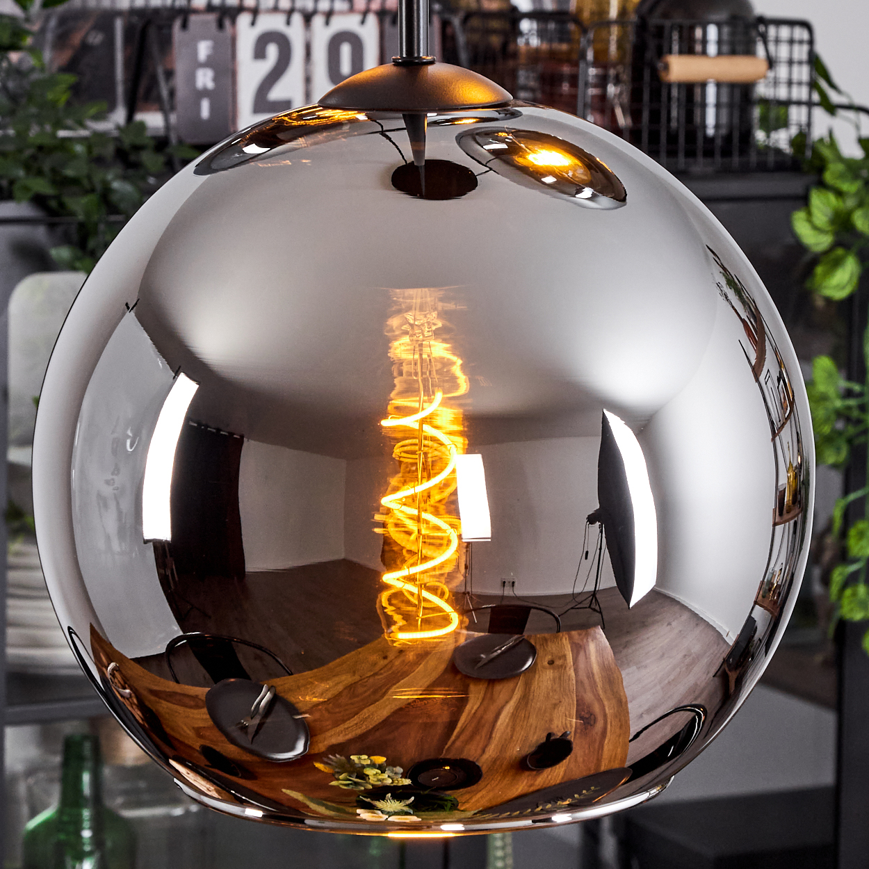 Nahaufnahme einer Pendelleuchte mit grauem Glasschirm. Eine Spirallampe reflektiert den Tisch darunter.