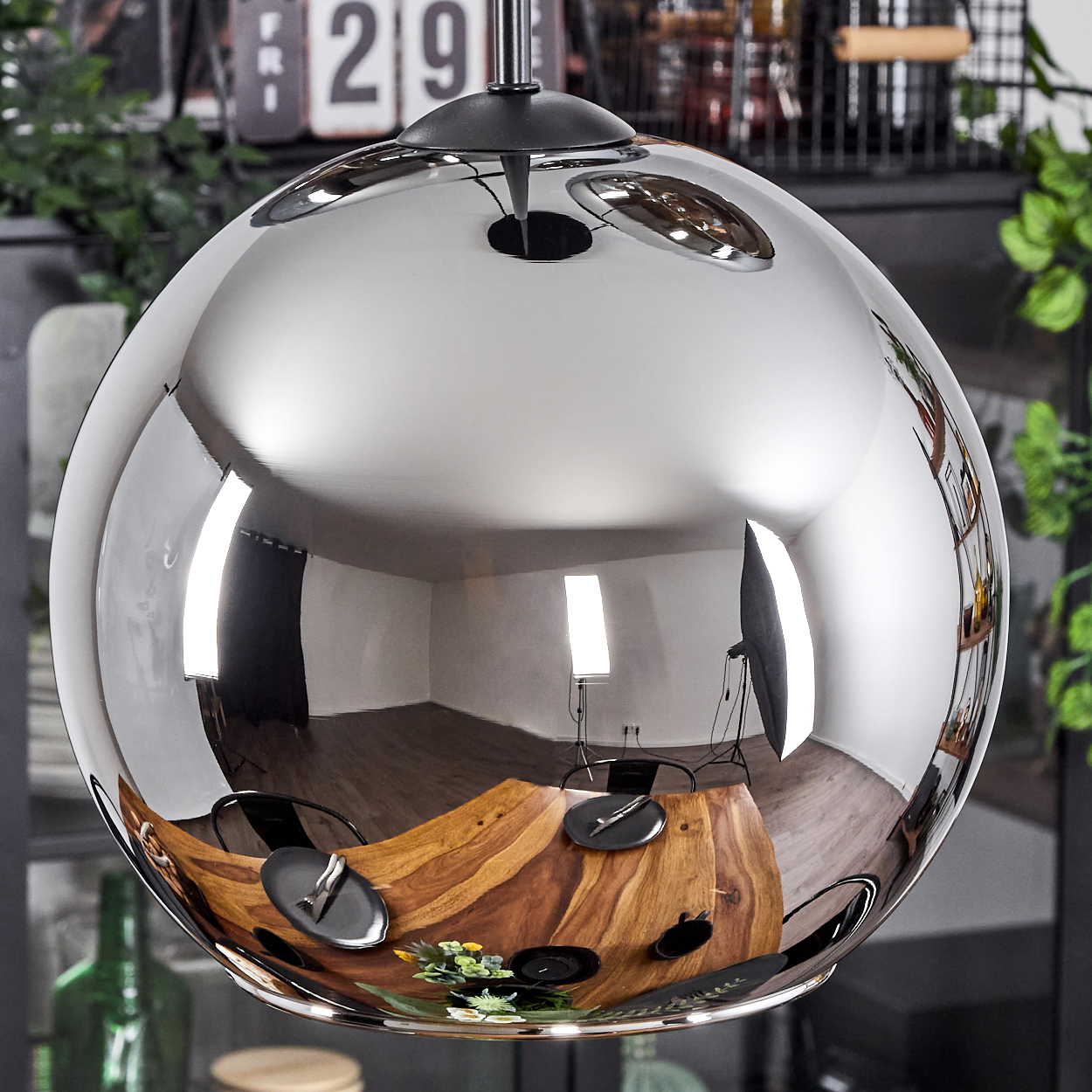 Eine große, glänzende, runde Lampe spiegelt den Essbereich mit einem Holztisch und Stühlen wider.