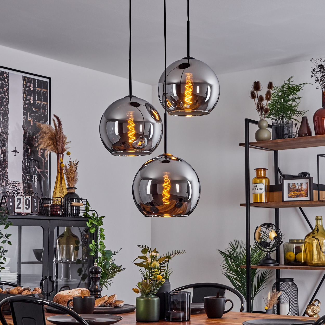 Drei Pendelleuchten mit grauen Glasschirmen hängen über einem Esstisch. Der Raum hat eine moderne Esszimmer-Einrichtung.