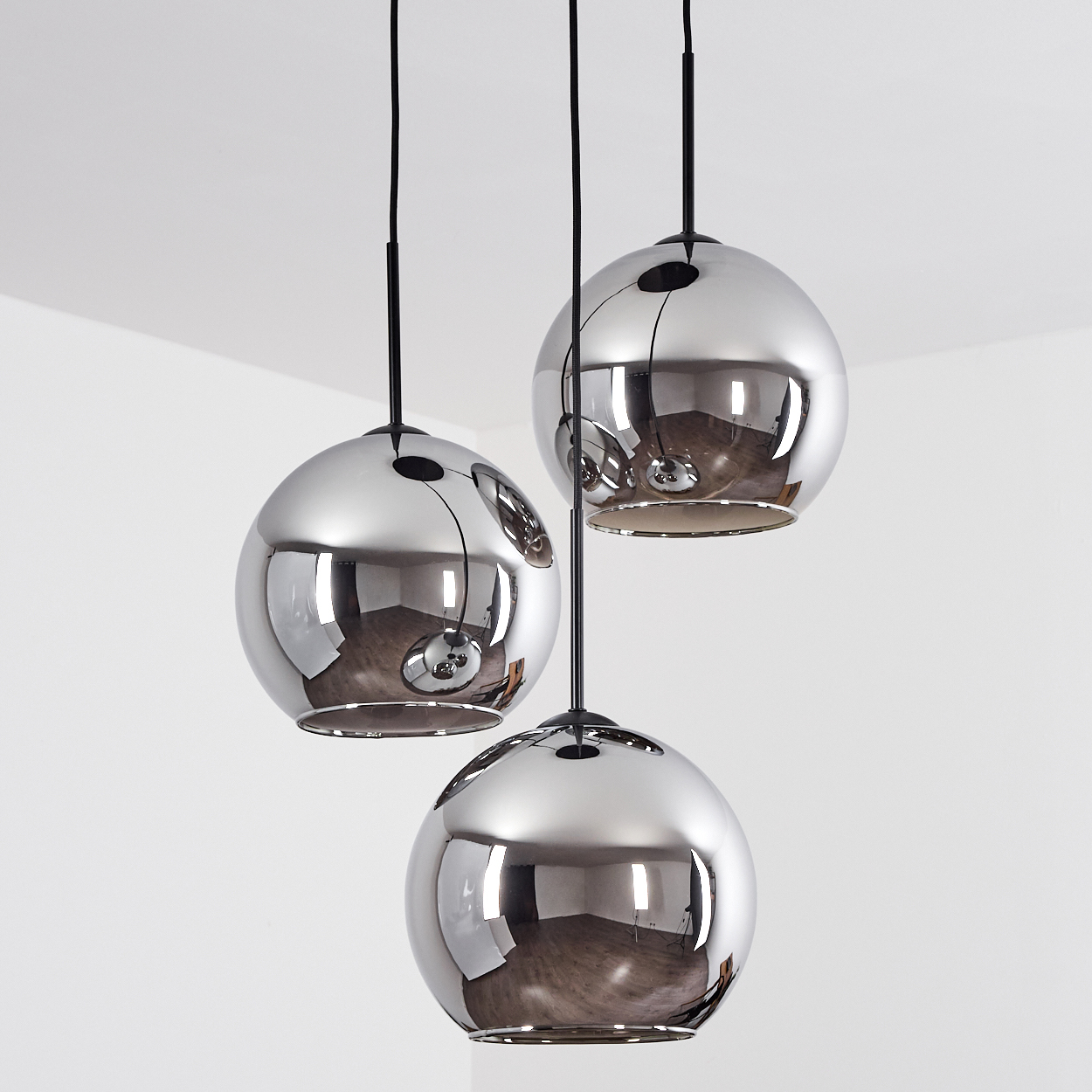 Drei Pendelleuchten mit glänzenden grauen Glasschirmen hängen in einer Ecke. Die Schirme sind kugelförmig und reflektierend.