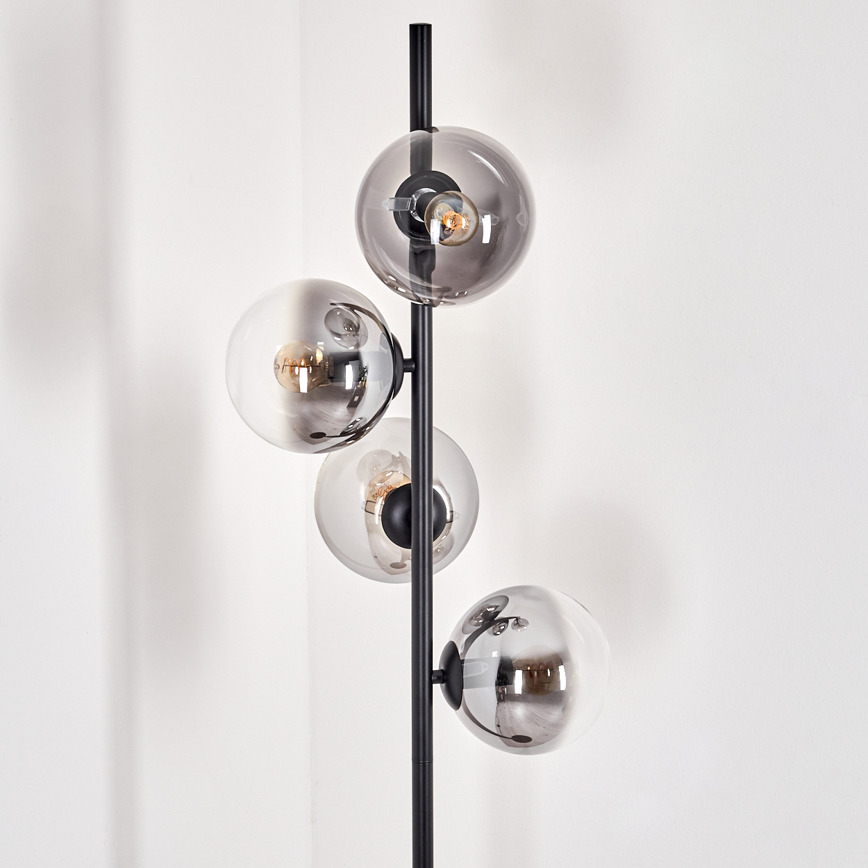 Eine Stehlampe mit vier Glaskugeln, einem schwarzen Pfosten und einem weißen Hintergrund.