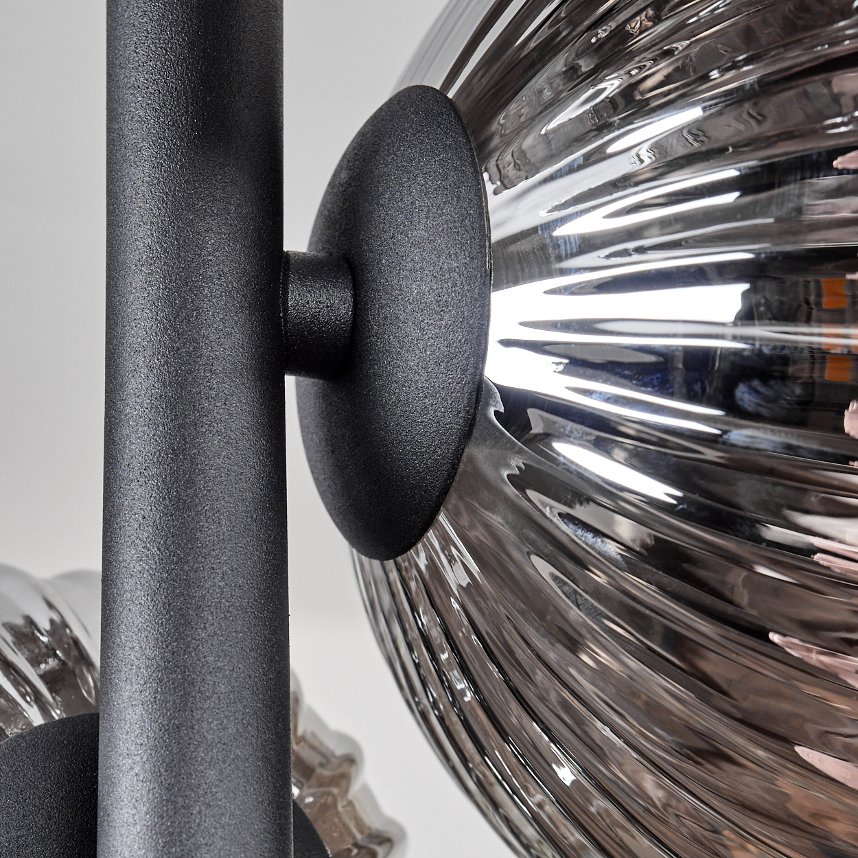 Nahaufnahme einer schwarzen Lampenfassung mit einem kugelförmigen, geriffelten Glasschirm. Das Licht spiegelt sich im Glas.