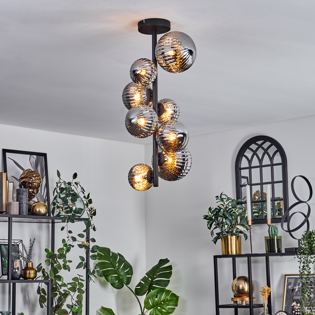 Ein Kronleuchter mit neun kugelförmigen Lichtern, die von der Decke hängen. Wohnraum mit Regalen und Dekoration.