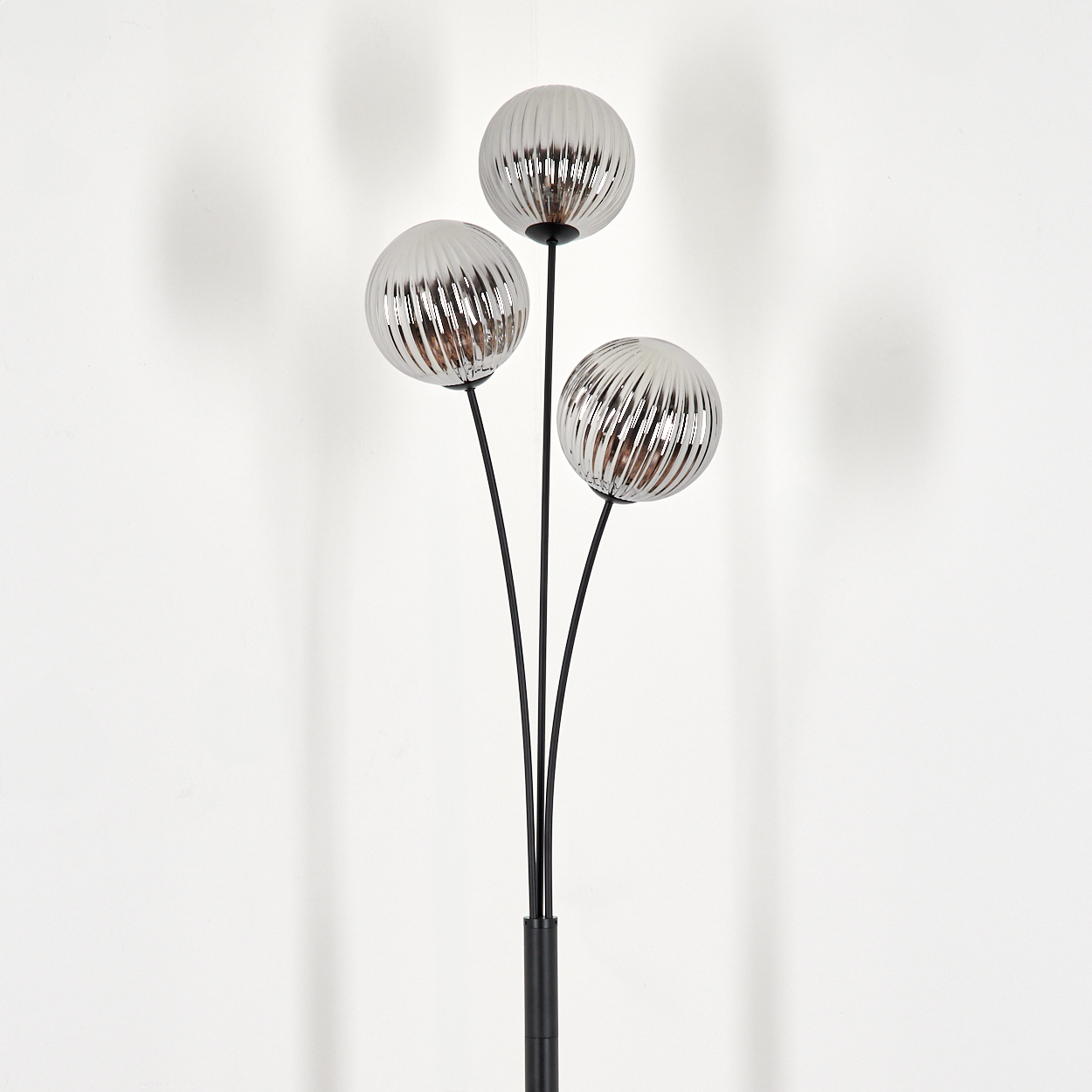 Drei Kugelschirme auf einer schwarzen Stehlampe. Der Hintergrund ist eine weiße Wand.