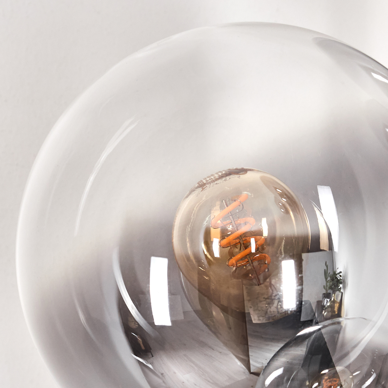 Nahaufnahme eines Glasschirms mit sichtbarer Glühbirne. Das Glas ist rauchgrau. Der Hintergrund ist eine weiße Oberfläche.