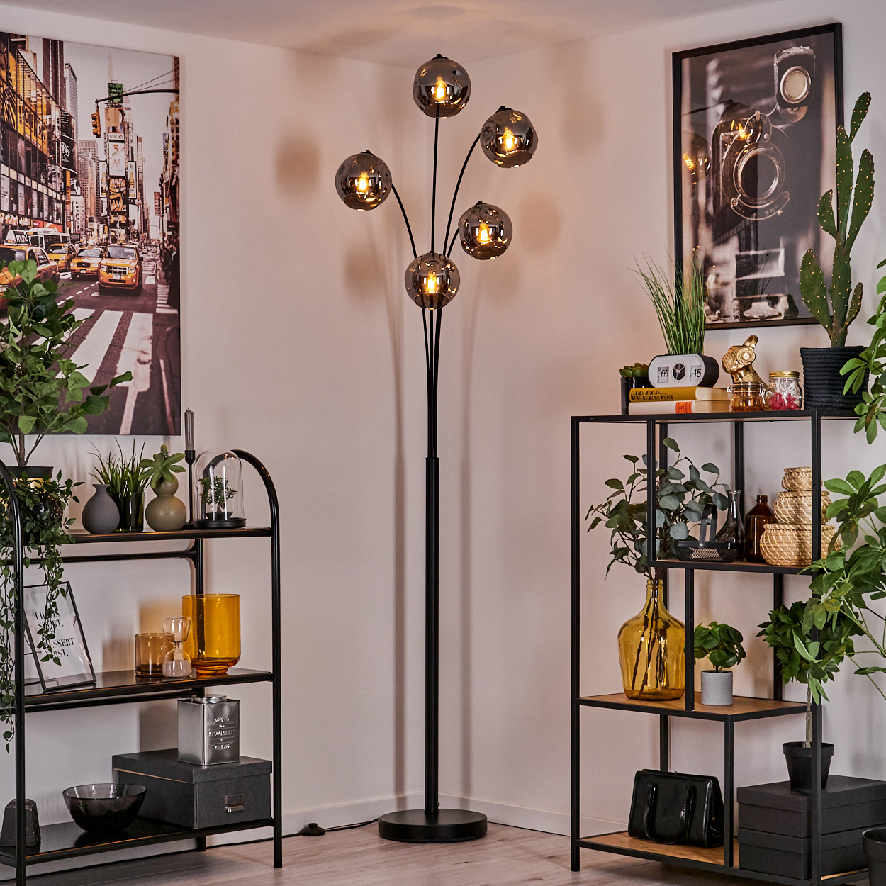 Ein Raum mit einer schwarzen Stehlampe mit fünf Glaskugelschirmen, Regalen, Pflanzen und Bildern.