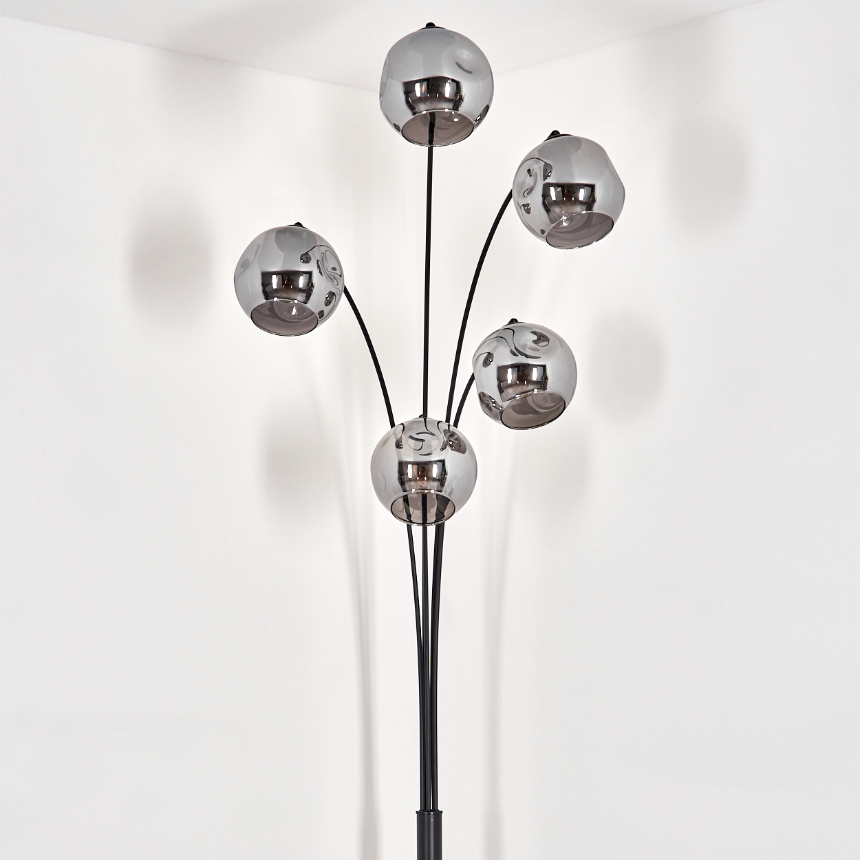 Eine Stehlampe mit fünf kugelförmigen Schirmen. Die Schirme sind silberfarben, der Sockel ist schwarz. Der Hintergrund ist eine weiße Wand.