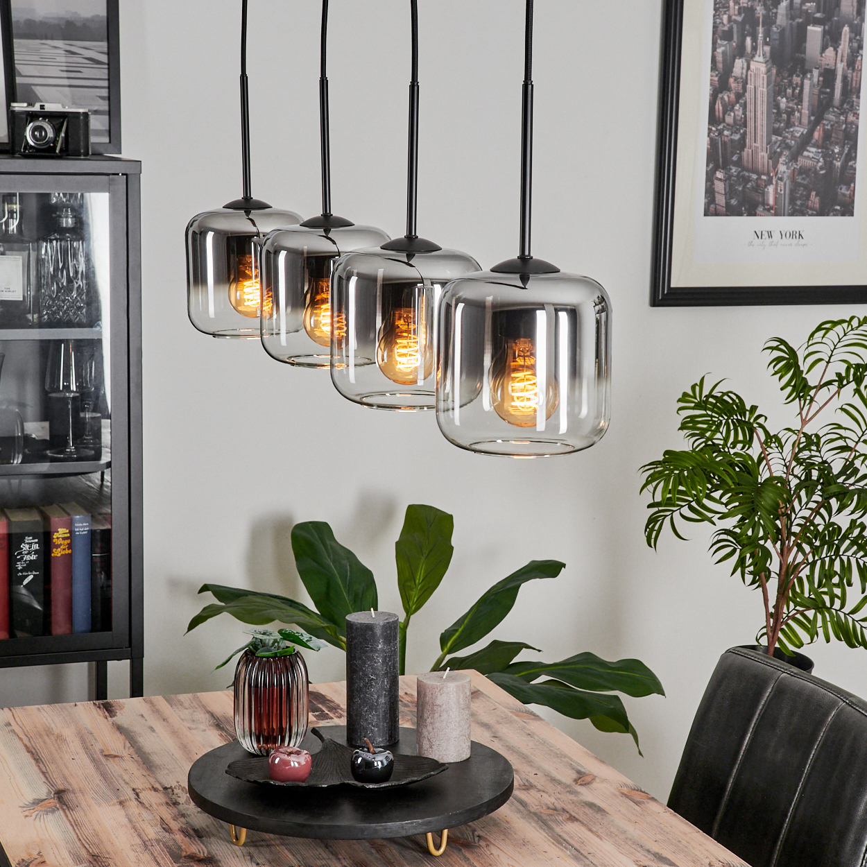 Ein Esszimmer mit einem Holztisch, Kerzen und vier Pendelleuchten mit klaren Glasschirmen darüber.