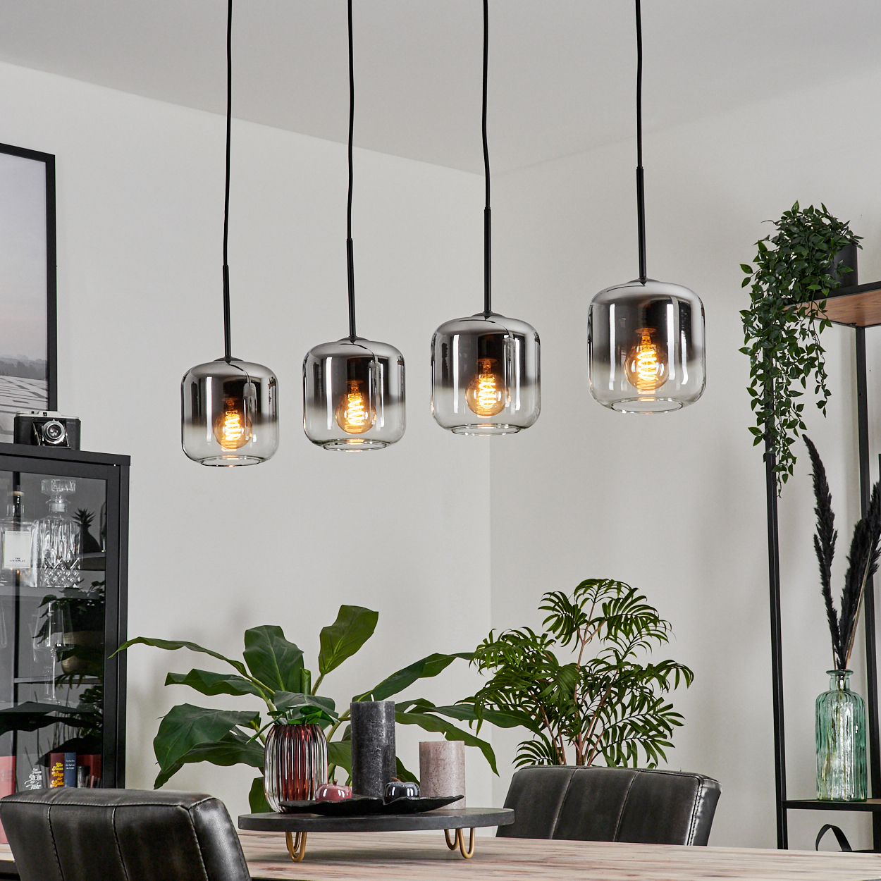 Ein Esszimmer mit vier Pendelleuchten mit klaren Glasschirmen, die über einem Holztisch hängen.