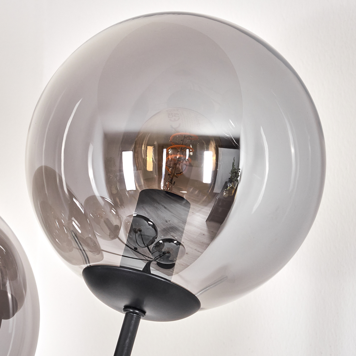 Nahaufnahme eines Glasschirms mit sichtbarer Glühbirne. Das Glas ist rauchgrau. Der Hintergrund ist eine weiße Wand.