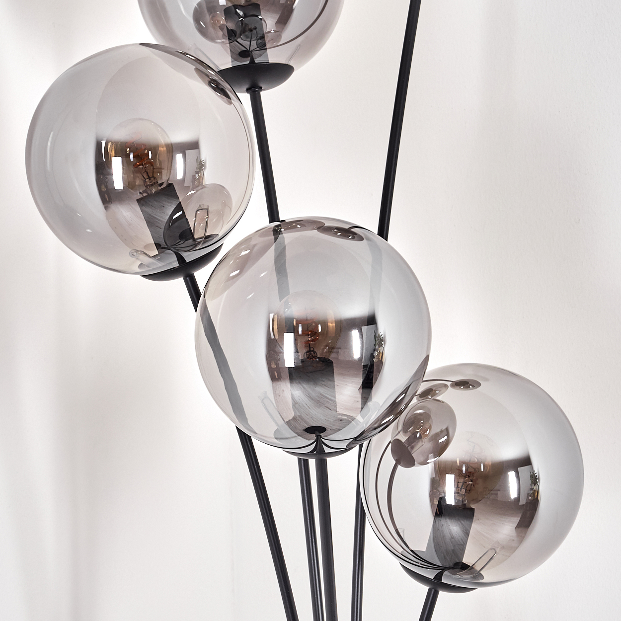 Eine Stehlampe mit fünf kugelförmigen, grau getönten Lampenschirmen. Die Lampe steht vor einer weißen Wand mit Schatten.