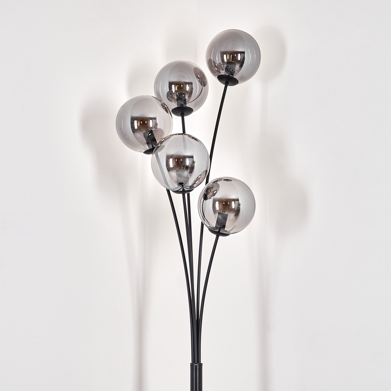 Eine Stehlampe mit fünf kugelförmigen, grau getönten Lampenschirmen. Die Lampe steht vor einer weißen Wand.