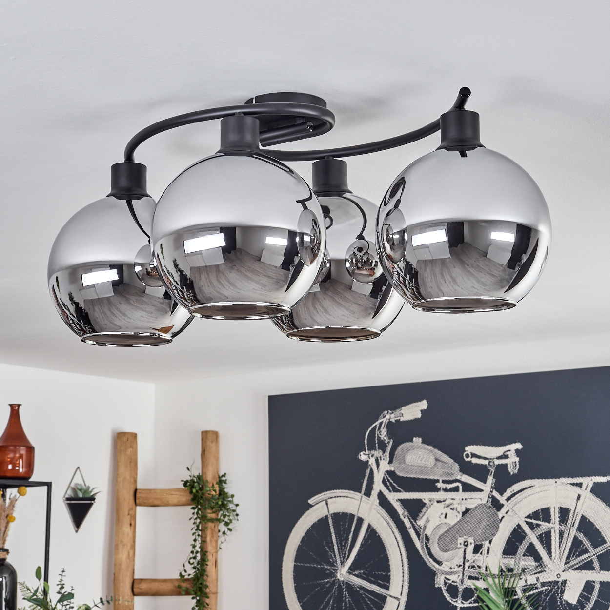 Deckenlampe mit vier Chromkugeln. Der Hintergrund hat Deko, eine Holzleiter und ein schwarz-weißes Fahrradkunstwerk.