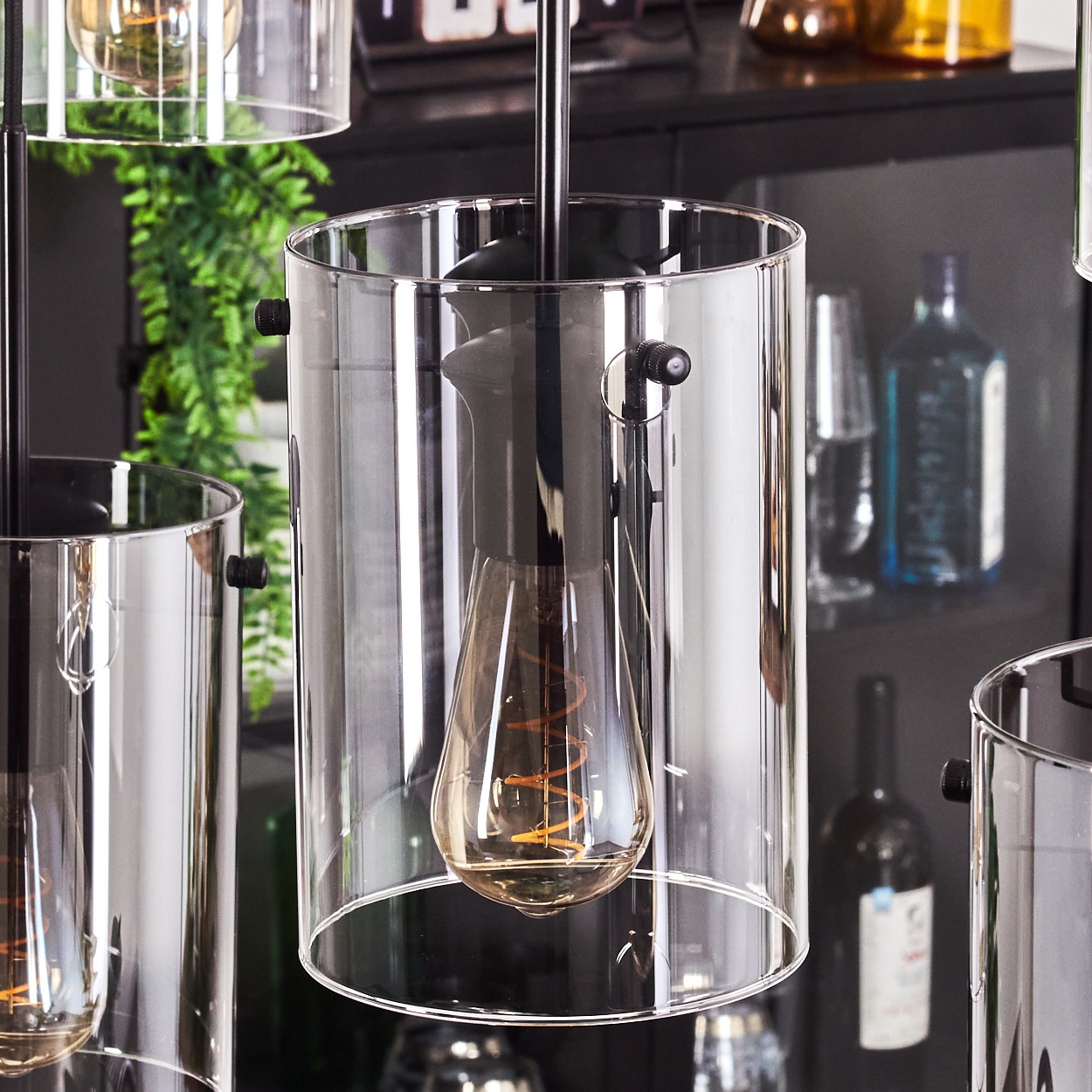 Nahaufnahme einer Lampe mit einem Glaszylinderschirm und einer Glühbirne. Andere Lampen sind im Hintergrund sichtbar.