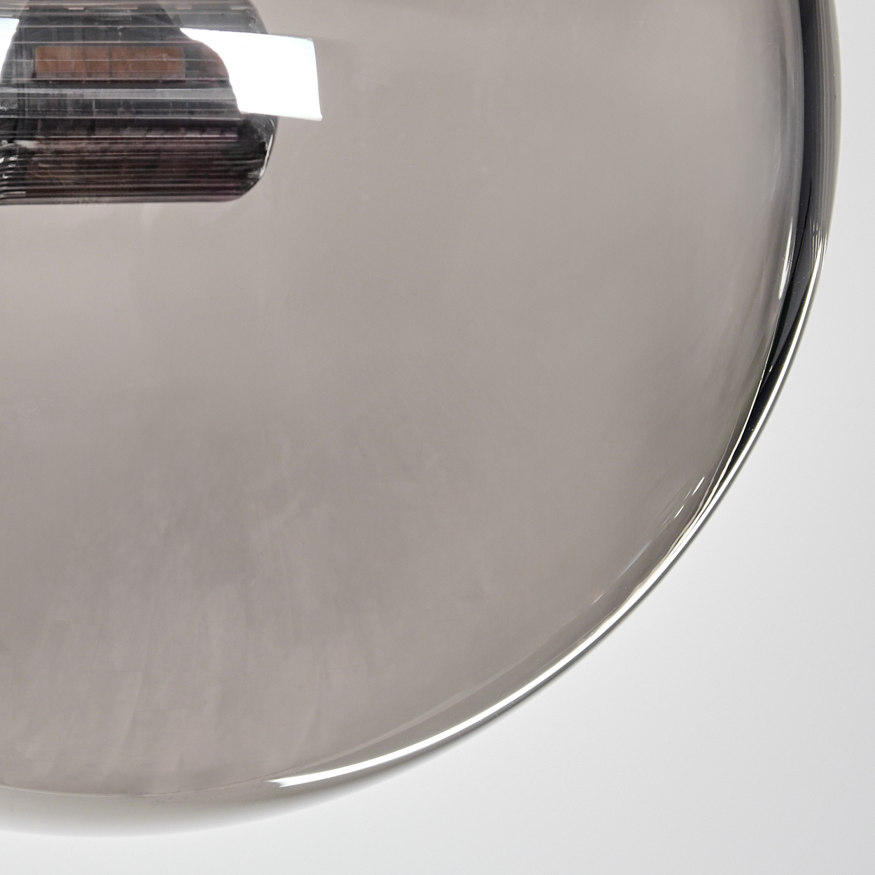 Nahaufnahme einer grauen Glaskugel. Der Hintergrund ist weiß und das Glas reflektiert.