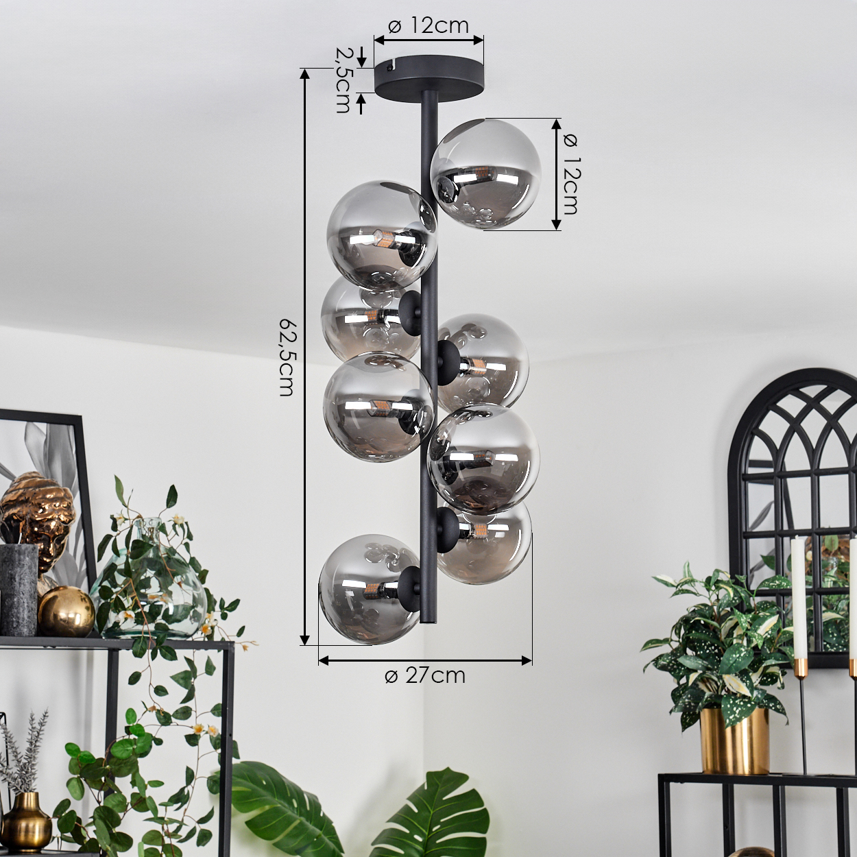 Eine schwarze, vertikale Lampe mit kugelförmigen Silberschirmen. Die Lampe befindet sich in einem Raum mit Pflanzen und Dekor.