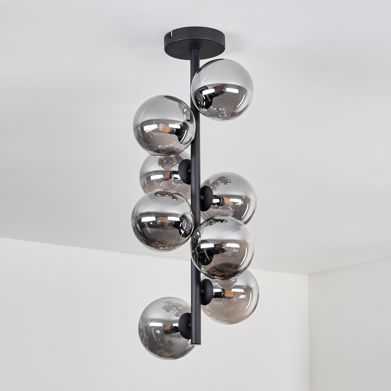 Eine Deckenlampe mit einer schwarzen Stange, die mehrere silberne Kugeln hält. Die Lampe befindet sich an einer weißen Decke.
