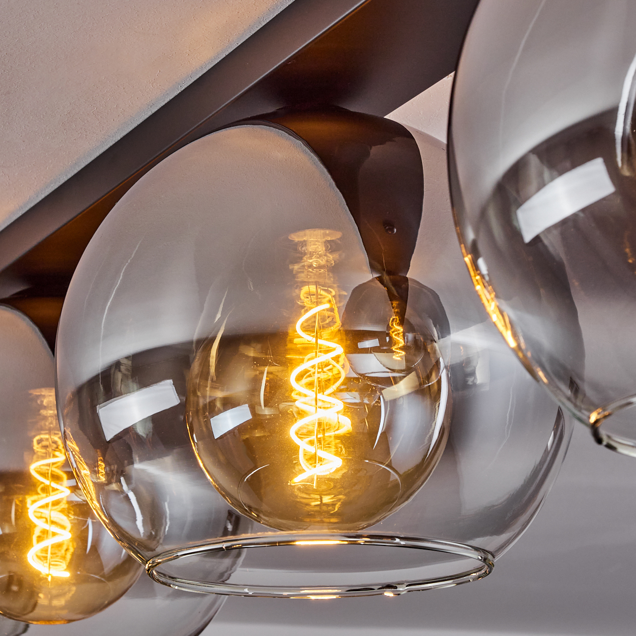 Nahaufnahme einer Deckenlampe mit drei Glaskugeln, jede mit einer leuchtenden Wendelglühbirne.